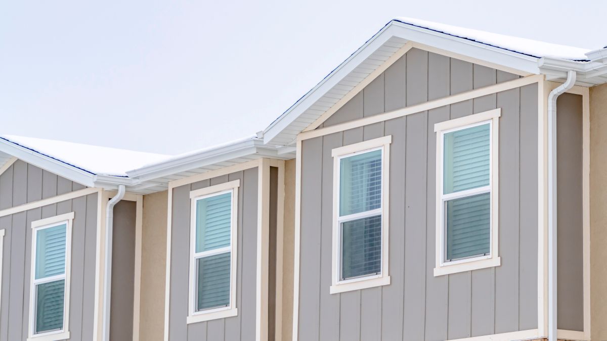 Panorama Snowy Roof Brick Wall And Vertical Siding At Exterior Of Townhome Against Sky