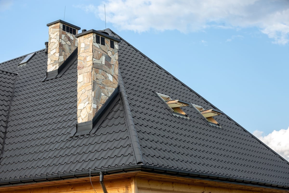 Log House With A Roof Made Of Metal Tiles And Stone Chimneys.