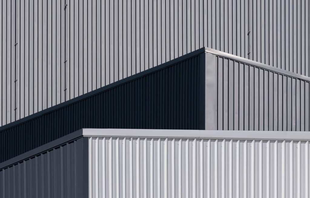 Sunlight And Shadow On Surface Of Gray And White Corrugated Metal Industrial Buildings
