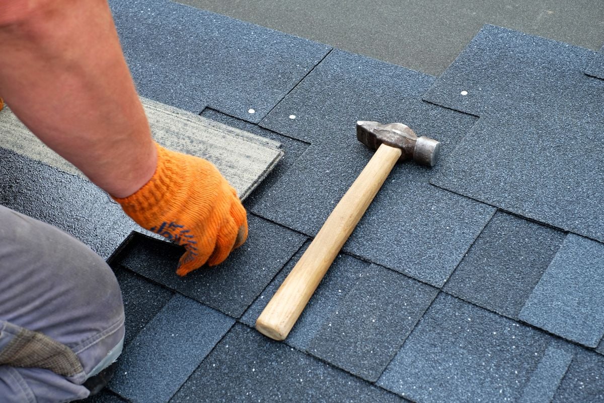 Contractor Hands Installing Bitumen Roof Shingles Using Hammer