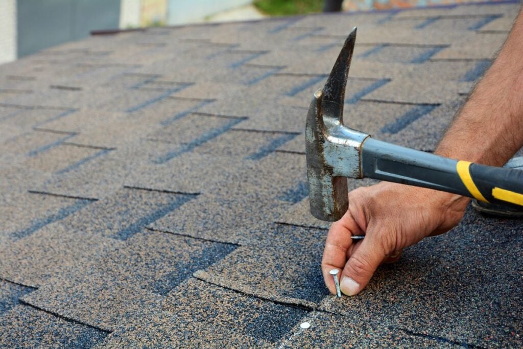 How to Choose a Roofing Contractor. Roofer Is Hammering A Nail In The Roof Shingles