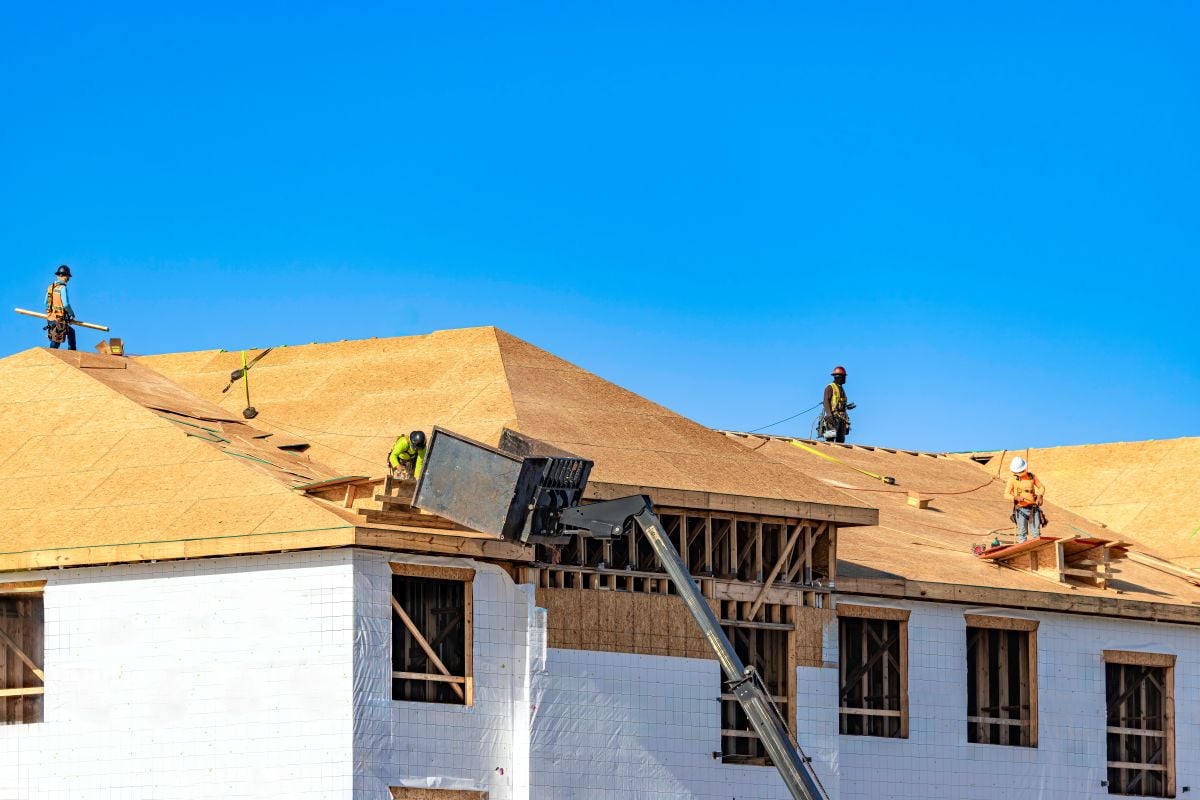Roofers And Construction Crew Installing Plywood Sheathing On New Building Roof