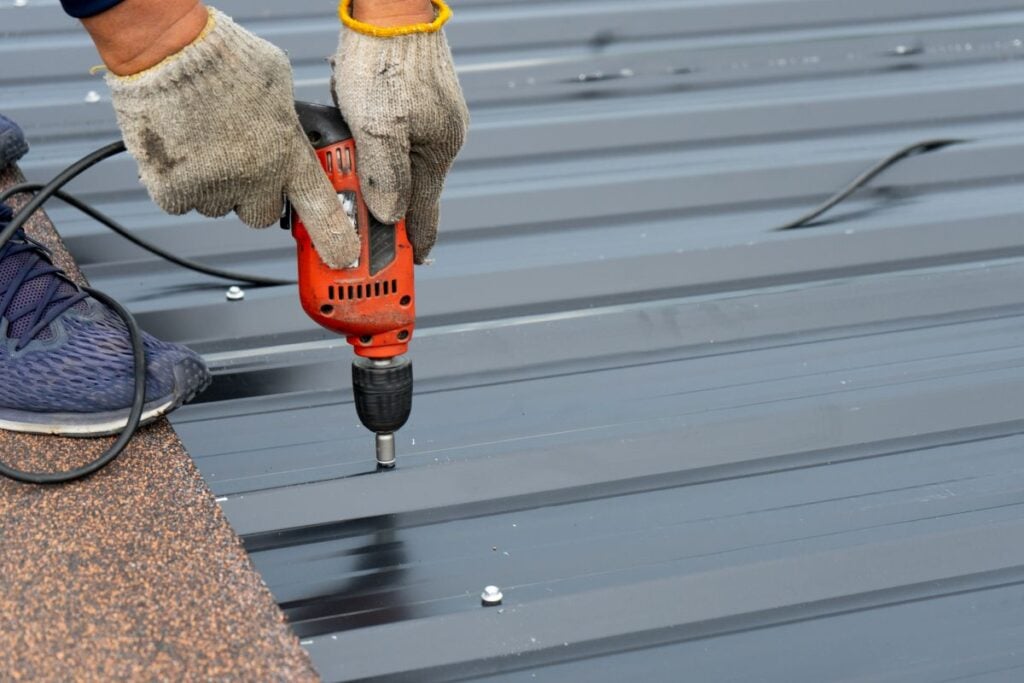 Workers Installing The Metal Sheet Roof By Electrical Drilling Machine. Metal Roofing Repair