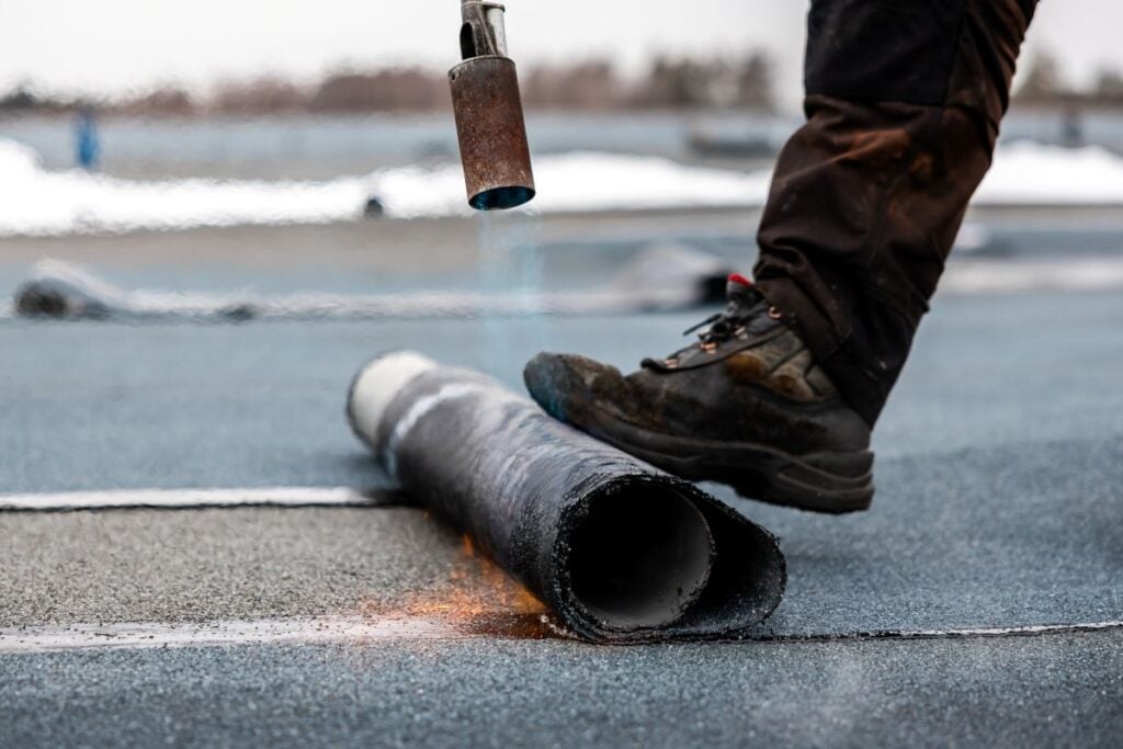 Professional Roofer At Work Securing Rolled Tar Paper With A Blowtorch On A Flat Roof Installation Process